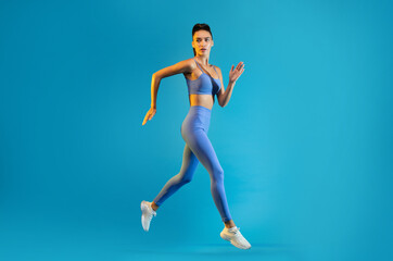 Fototapeta na wymiar Fitness Female Jumping Posing In Mid Air Over Blue Background