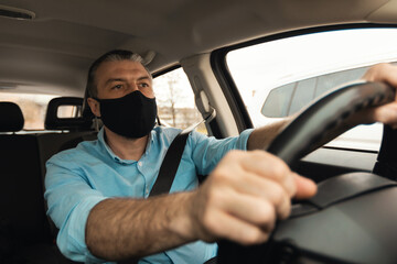 Confident man in facemask driving new car in city