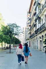 Fototapeta na wymiar Vertical shot of two unrecognizable women back to back with bags walking around the city.