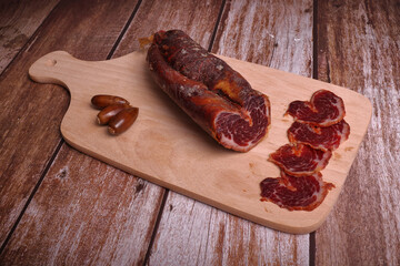 Iberian tenderloin on cutting board and dark wood table, adorned with acorns.