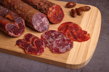 Iberian sausage, Iberian chorizo and Iberian tenderloin on cutting board and dark gray table.