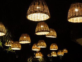 Many lamps with wicker lampshades illuminate the dark bamboo alley in the park.