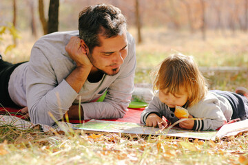 Father and son reading book lying on green grass in park. Concept of happy family relations and carefree leisure time
