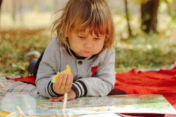 Cute boy in summer park lying on blanket and reading book