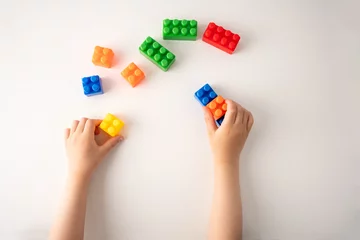 Fotobehang Lego High angle shot of a child is playing with colorful construction blocks and kid hands with bricks toy on white background educational toy.  © cunaplus