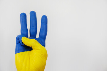 Man's hand painted in colors of Ukrainian flag showing a traditional trident hand gesture symbolizing national coat of arms. Copy space, close up, background.