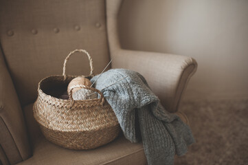 Making homemade knitted sweater at home. Straw basket with yarn wool skein with knitted fabric on...