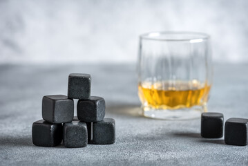 Closeup of whiskey stones and a glass of whiskey on a gray concrete table. Side view, selective...