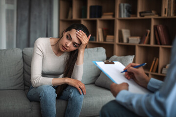 Obraz premium Sad young european lady hold her head with hand at consultation with male doctor psychologist with tablet