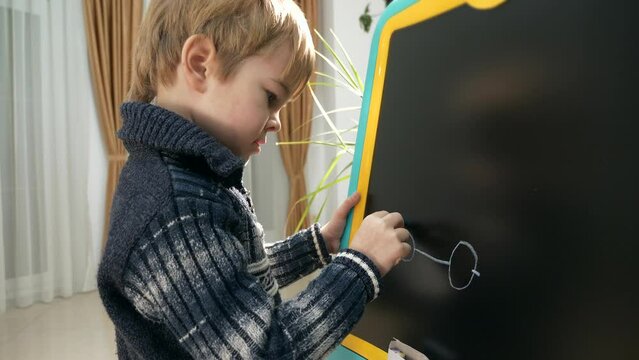 Little Boy Kid Draws Car with Chalk on Blackboard. Child Education at Home. Evening Room Interior. 2x Slow motion 60fps 4K