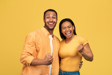 Excited young black man and woman gesturing YES, celebrating success on yellow studio background
