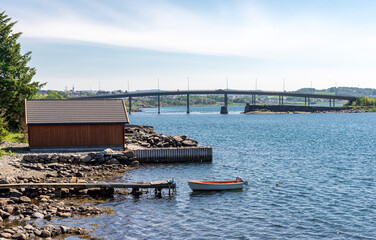 Rocky beach with a short wooden jetty and a small fishing boat near Hafrsfjord bridge, Tananger, Norway, May 2018