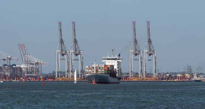 Southampton, England, UK. 2022. Small container carrier ship departing DP World, Southampton container port with backdrop of cranes and containers.