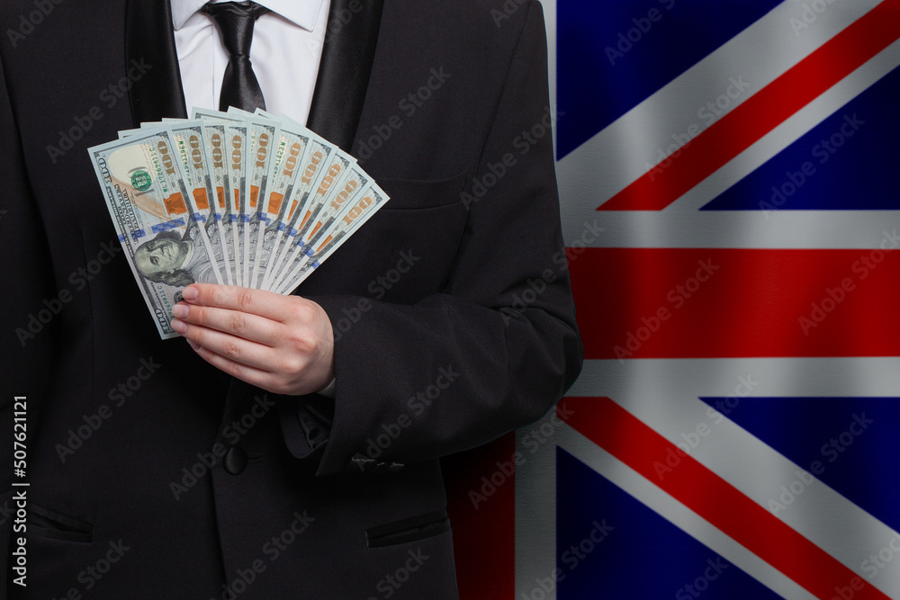 Wall mural UK business man hand with 100 US dollar bills banknotes money on flag of United Kingdom background