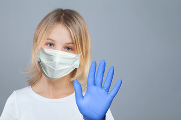 Pretty blonde child girl in medical facial mask showing stop gesture. Hand in blue nitrile glove