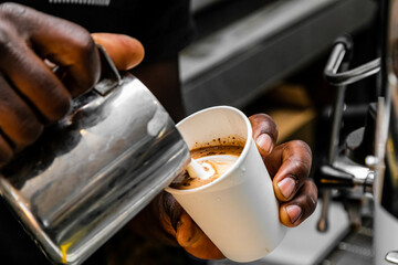 African Coffee Barista pouring a heart shape with milk foam.