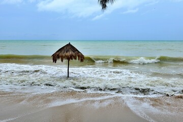 Thatch umbrella at the beach with strong waves crashing against the beach.