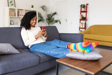 Millennial african american woman using mobile phone sitting on couch at home - Mixed race...