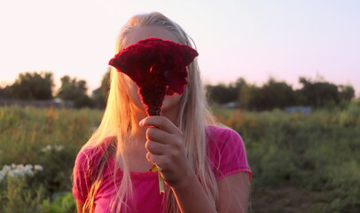 portrait of a blonde girl with a large flower at the face against the background of nature at...