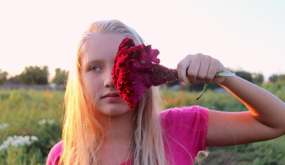 portrait of a blonde girl with a large flower at the face against the background of nature at...