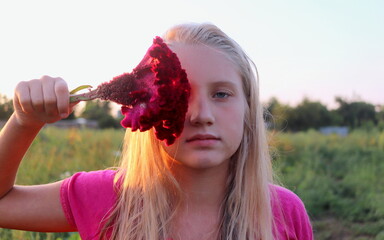 portrait of a blonde girl with a large flower at the face against the background of nature at...