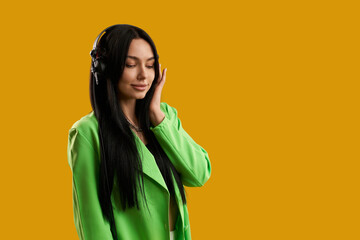 Smiling brunette woman with earphones listening music indoor. Front view of female music lover with closed eyes, enjoying sound, isolated on orange studio background. Concept of enjoyment.