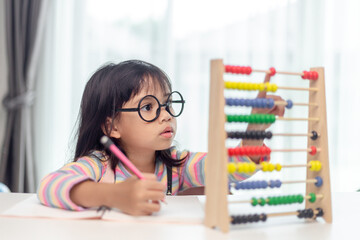 A young cute Asian girl is using the abacus with colored beads to learn how to count at home - obrazy, fototapety, plakaty