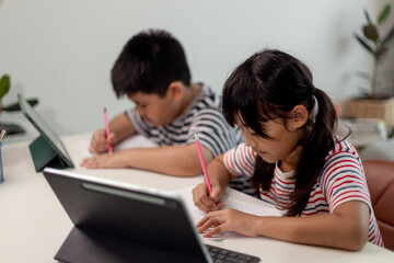 Asian boys and girls enjoy online learning by taking notes and using tablets at home.