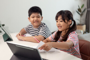 Fototapeta na wymiar Asian boys and girls enjoy online learning by taking notes and using tablets at home.