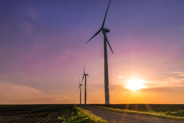 Two windmills standing tall in a mid-western field during a vibrant, colorful sunset.
