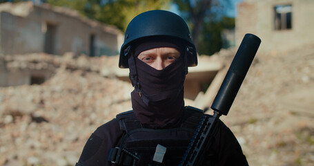 A Ukrainian soldier stands with a weapon near a destroyed house