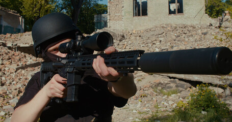 A soldier shoots a sniper rifle against the background of a destroyed house.