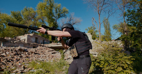 A soldier with a rifle goes to the reconnaissance, near the destroyed house