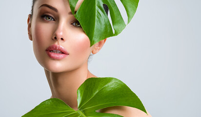 Beautiful woman with green leave near face and body.  Closeup girl's face with green leave. Skin...