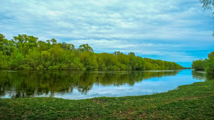 Beautiful spring green landscape with  flowing river and  fluffy clouds. Beautiful nature on spring. No people. Photo of a  summer landscape with a cloudy skies.