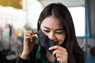 Take a close-up portrait of a beautiful Thai woman about to take off a black mask.