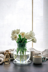 Home composition with a bouquet of tulips in a glass vase and candles.