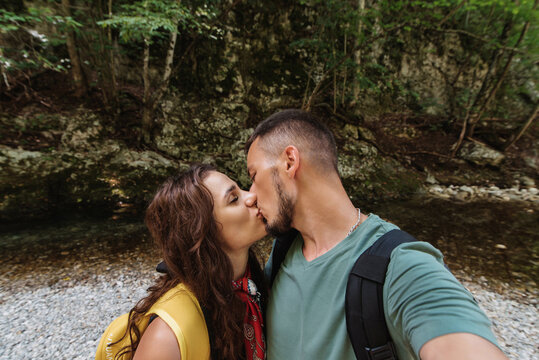 Selfie-portrait of a young couple in love kissing against a background of trees in a mountainous area. The concept of tourism, shared recreation