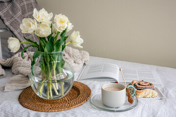 Cozy composition with a bouquet of flowers, coffee and a bun in bed.