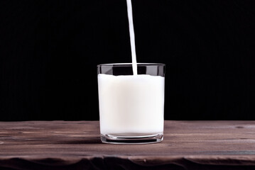 Milk. A glass of milk. Pours milk into a glass. A glass of milk on the table. Black background
