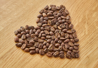 Black coffee beans seed in heart shape on brown wooden table, dark cofee arabica robusta roasted grain flavor aroma cafe, natural coffe shop background, top close up view from above,