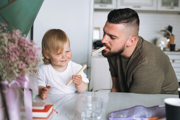 Happy father young man feeding and having fun with baby girl little daughter in kitchen at home