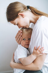 Vertical portrait of young woman mother kissing baby girl daughter on hands at home