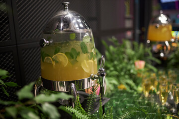 Lemonade in a dispenser on a table decorated with fresh herbs and flowers 