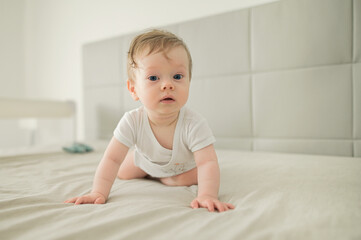 Fototapeta premium A happy smiling little cute toddler baby boy trying to crawl and playing at home on the bed. Eco friendly toys and motherhood concept.