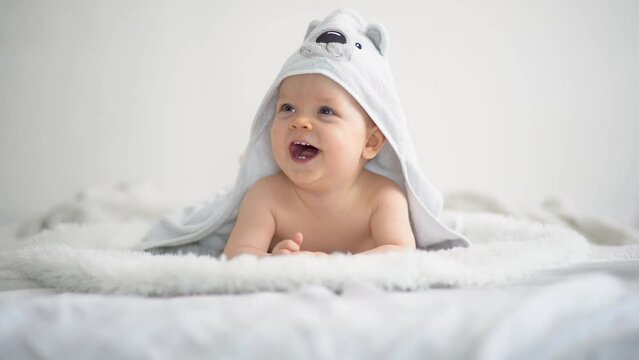 Cute funny little baby boy, relaxing in bed after bath, laughing happily