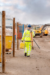 Site engineer wearing a bright hi-viz suit and safety boots walking on construction site carrying...