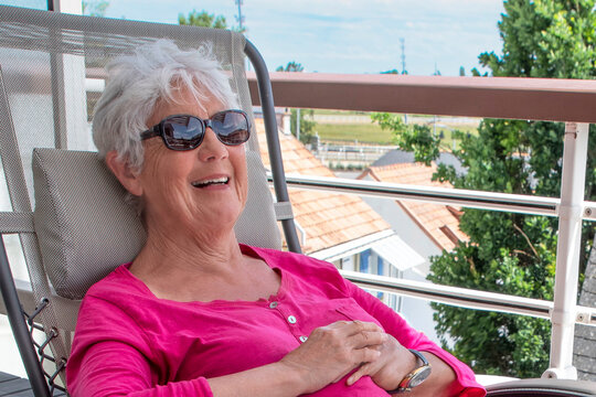 A smiling senior woman sitting in a deck chair on the terrace of a flat
