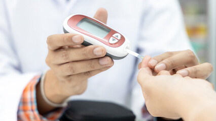 Asian woman pharmacist taking blood sample from asian girl finger for glucometry. Diabetes. Glucose control. Glucometer. Blood glucose level. Device with lancet for glucometry.