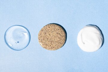 Drops of cosmetic products on a blue background. Body cream, clear liquid gel and coffee scrub.